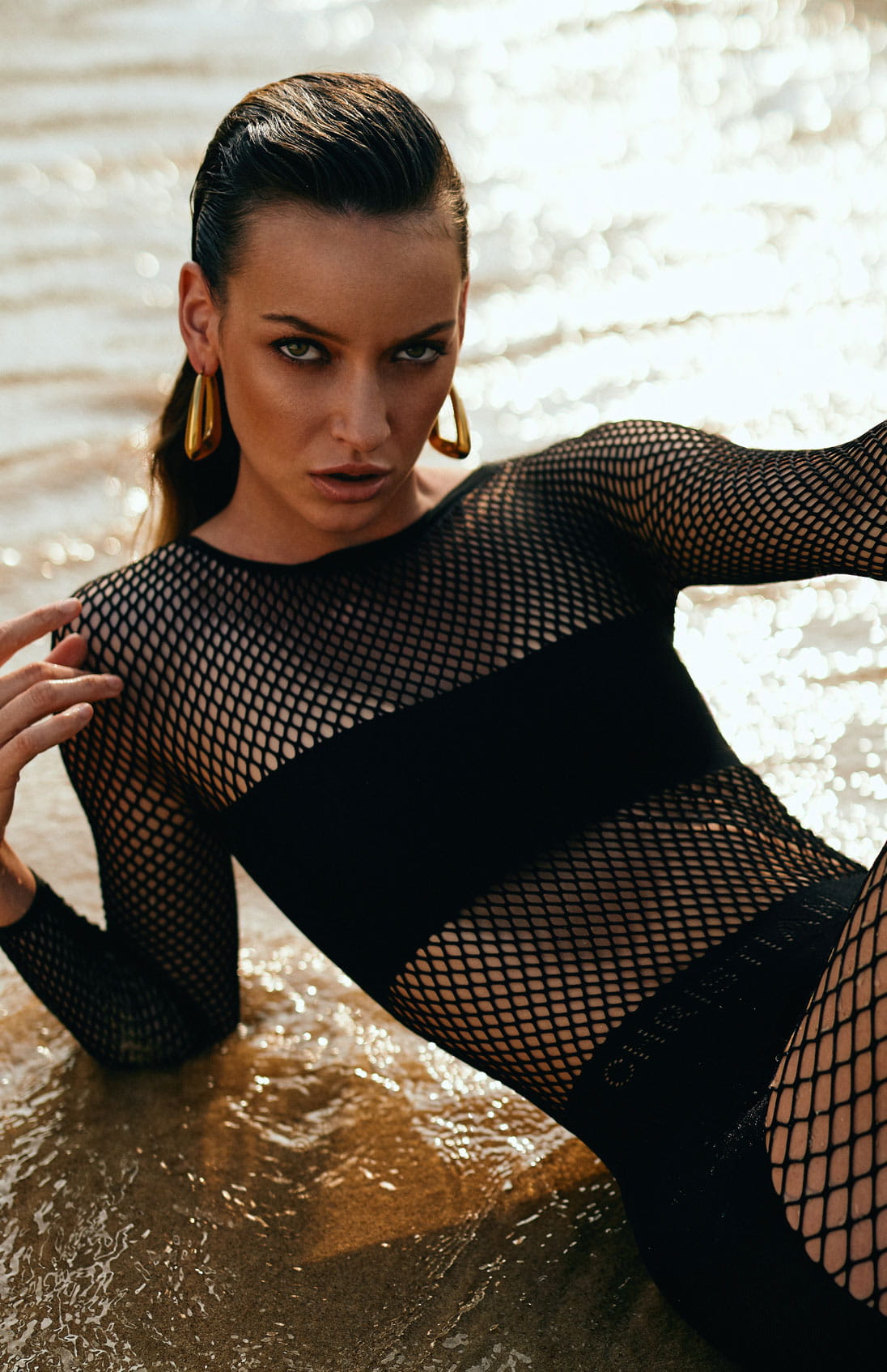 A model poses on the beach in a Dior mesh jumpsuit