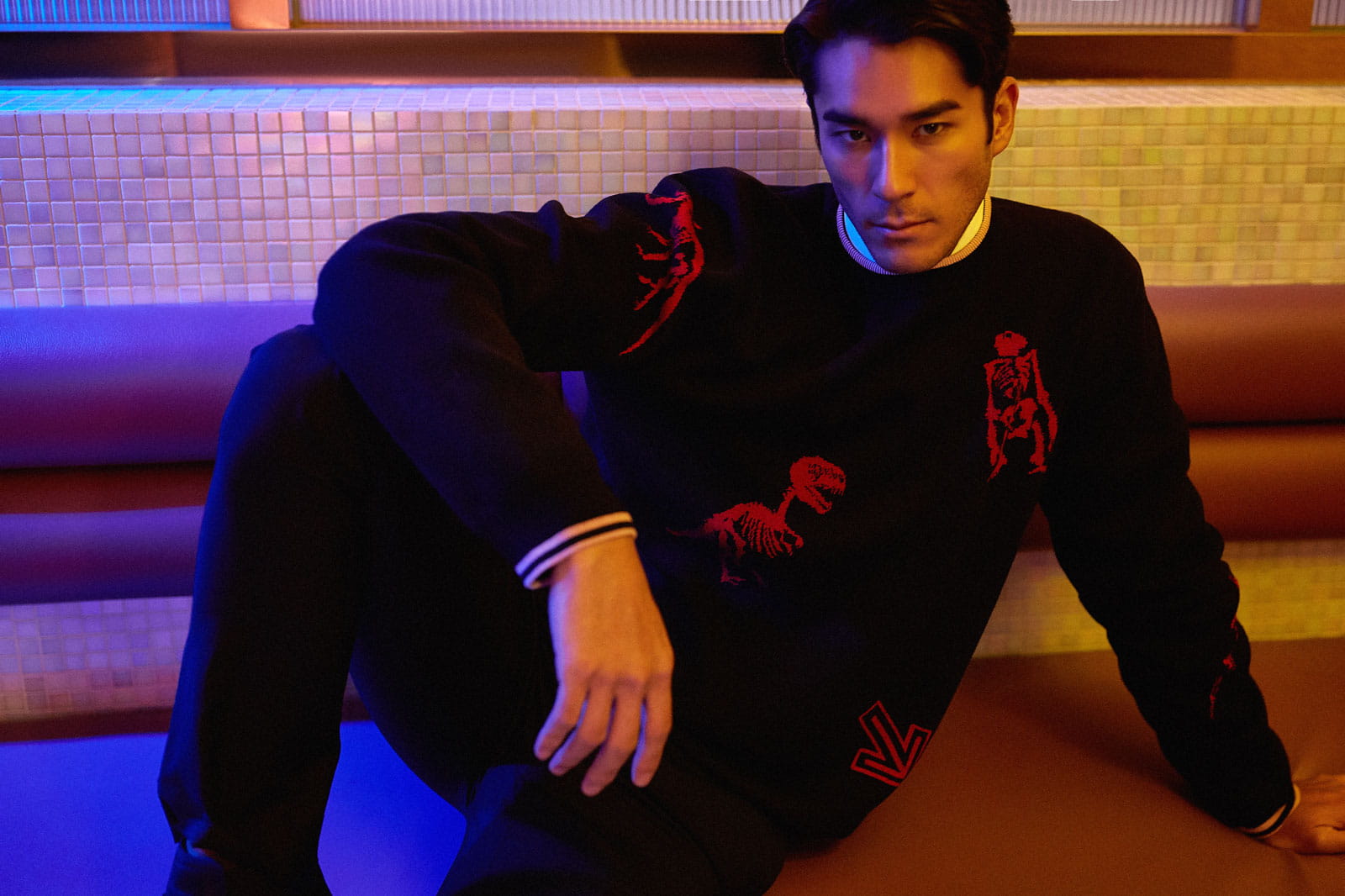 A model lounges on the seats of a diner wearing a dinosaur motif Lanvin sweater