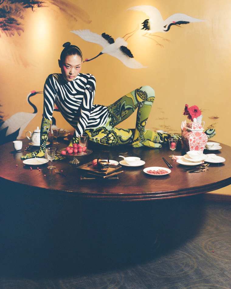 A model lies on a table wearing a zebra-print Moncler bodysuit