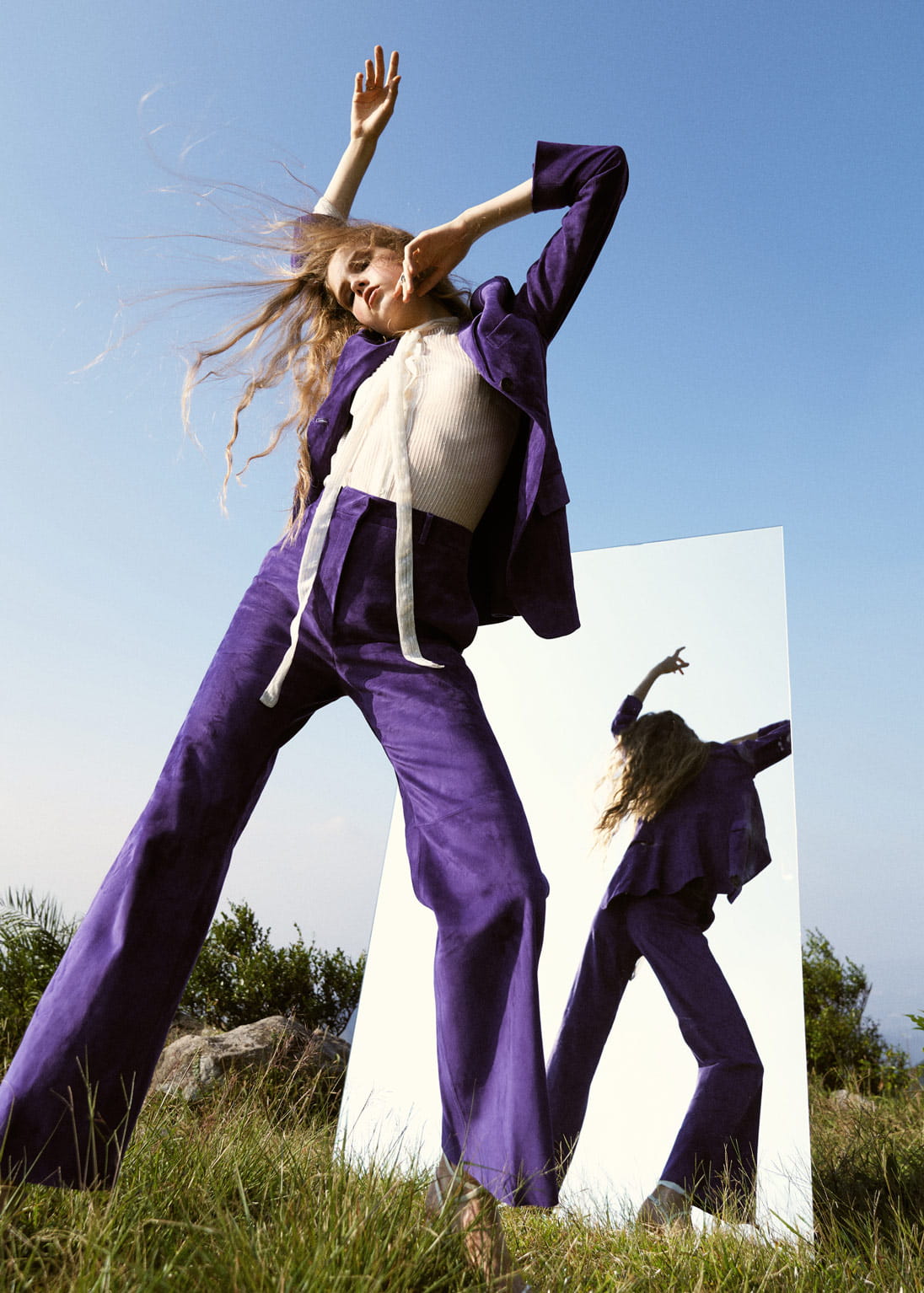 A model poses in front of a mirror on a grassy hill wearing a purple Salvatore Ferragamo suit