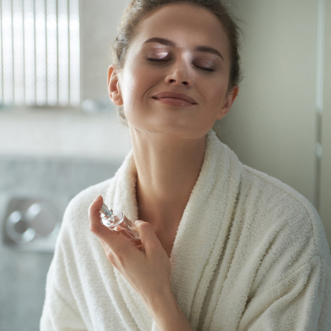 A smiling woman spraying scent on her neck