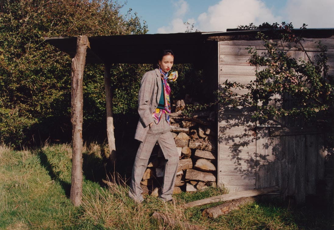 A model in a pant suit poses next to a pile of logs