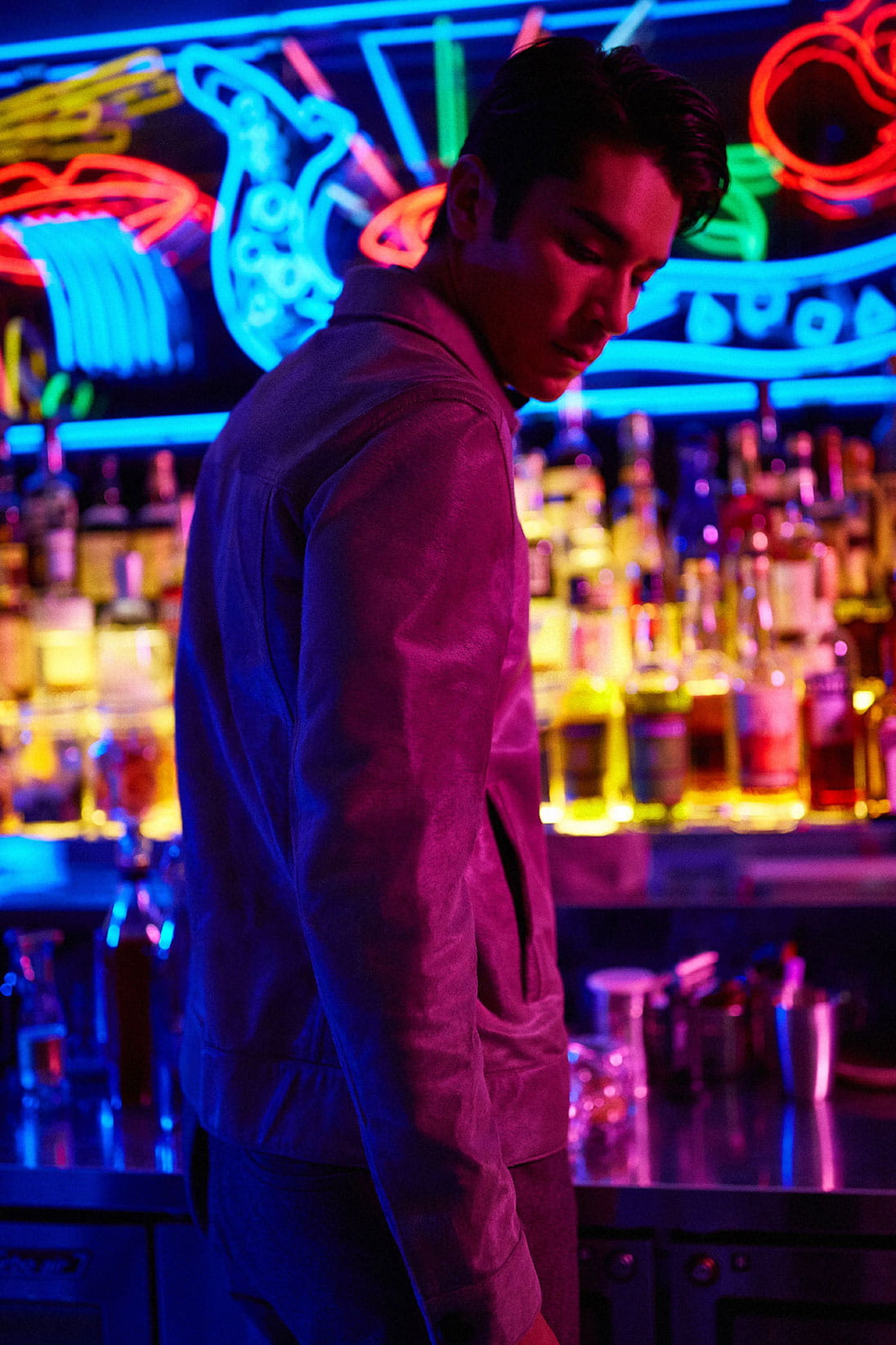 A model stands at a neon-lit bar wearing Salvatore Ferragamo and Hermès