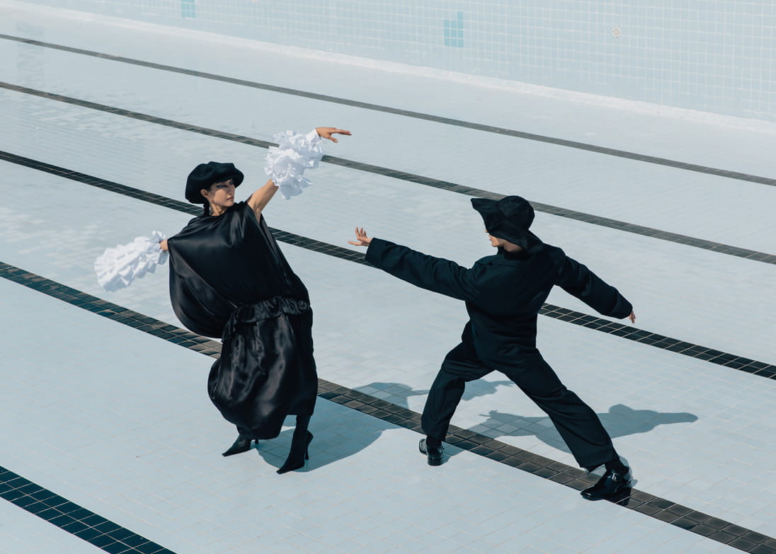 A female model wears ruffled statement sleeves from Comme des Garcons, and a male model wears soft black tailoring