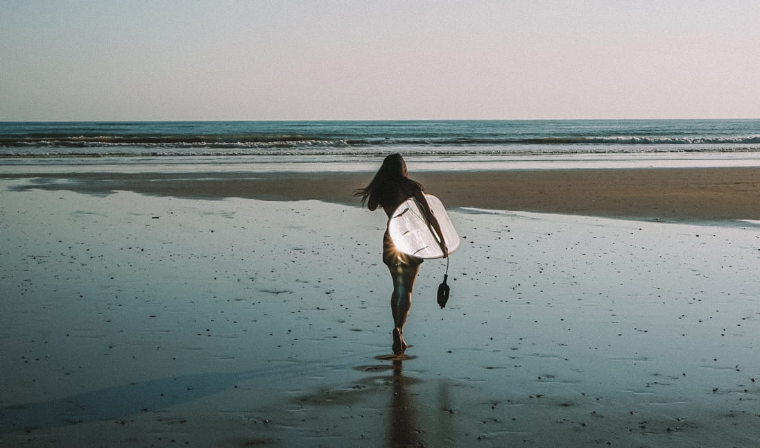 A surfer carries her surfboard to the water
